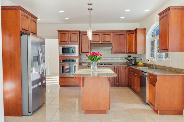 kitchen with appliances with stainless steel finishes, light stone counters, sink, decorative light fixtures, and a center island