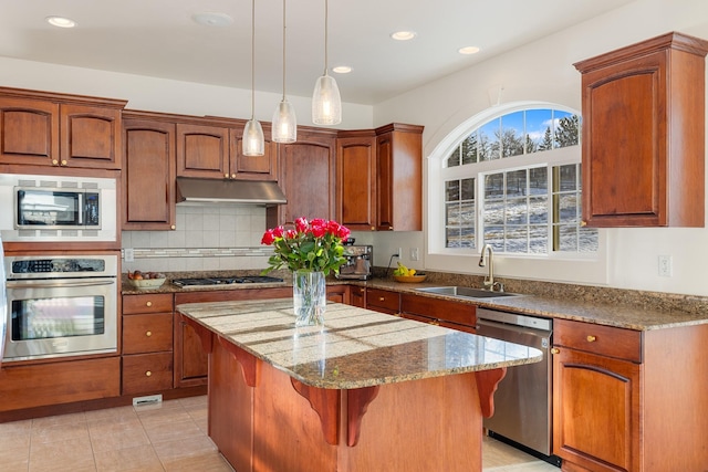 kitchen with sink, light stone countertops, appliances with stainless steel finishes, tasteful backsplash, and a kitchen island