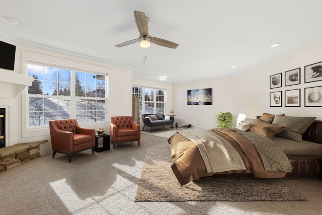 carpeted bedroom with multiple windows, a stone fireplace, ceiling fan, and crown molding