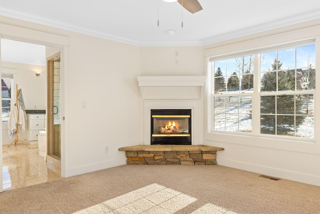 unfurnished living room featuring a stone fireplace, crown molding, carpet floors, and ceiling fan