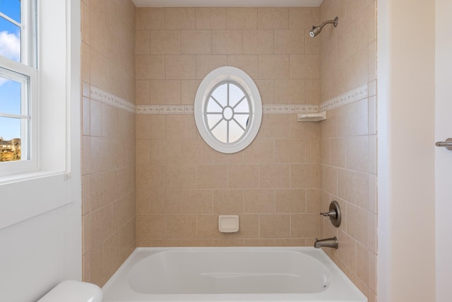 bathroom featuring toilet, plenty of natural light, and tiled shower / bath