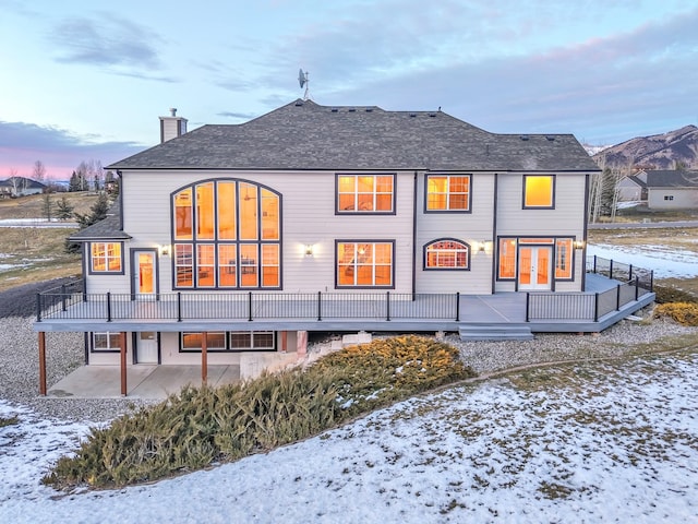 snow covered back of property featuring a patio area and a wooden deck