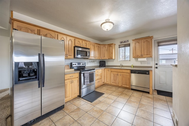 kitchen featuring light brown cabinetry, a textured ceiling, stainless steel appliances, sink, and light tile patterned floors