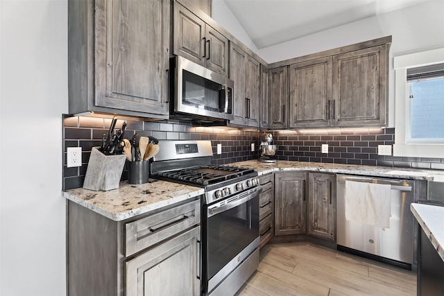 kitchen with dark brown cabinetry, lofted ceiling, tasteful backsplash, appliances with stainless steel finishes, and light stone countertops