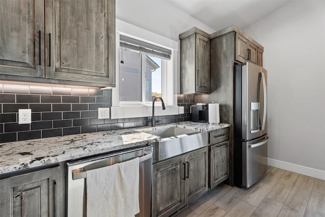 kitchen with sink, decorative backsplash, light stone counters, stainless steel appliances, and light wood-type flooring