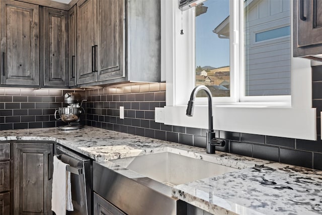 kitchen featuring light stone countertops, dark brown cabinets, sink, and decorative backsplash