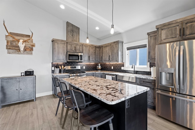 kitchen with a kitchen island, appliances with stainless steel finishes, decorative light fixtures, tasteful backsplash, and light stone counters