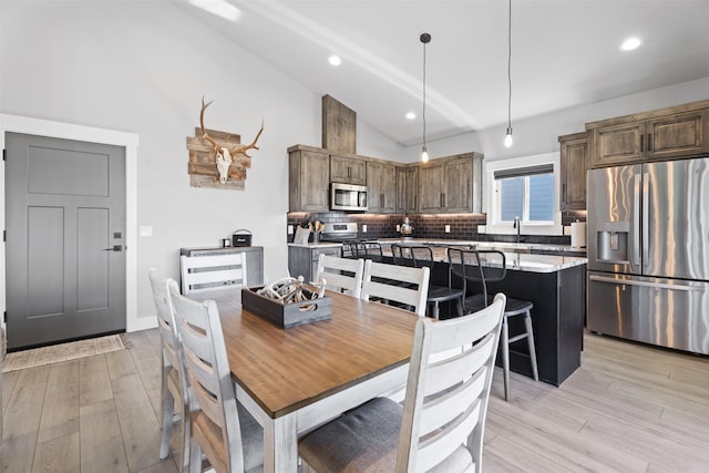 dining area featuring high vaulted ceiling, sink, and light hardwood / wood-style floors