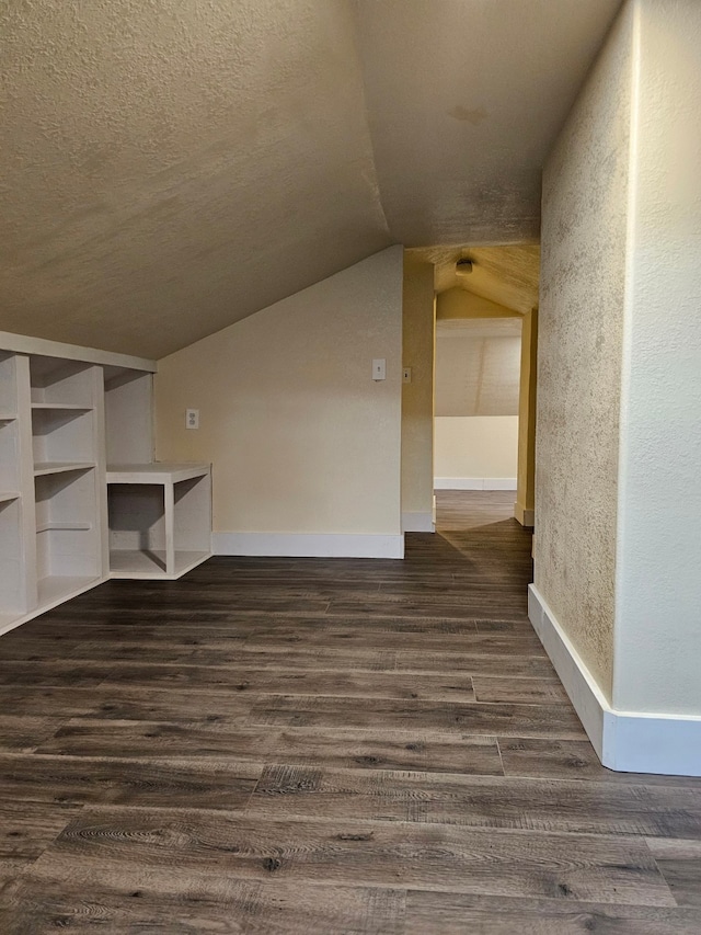 interior space with a textured ceiling, dark hardwood / wood-style floors, and vaulted ceiling