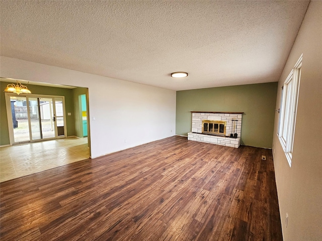 unfurnished living room with a chandelier, hardwood / wood-style flooring, a stone fireplace, and a textured ceiling