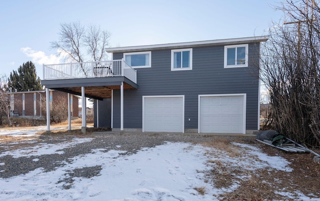 snow covered back of property with a wooden deck and a garage