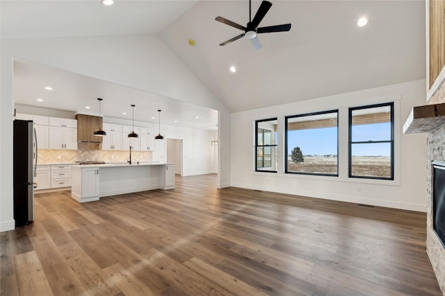 unfurnished living room with high vaulted ceiling, ceiling fan, a stone fireplace, and wood finished floors