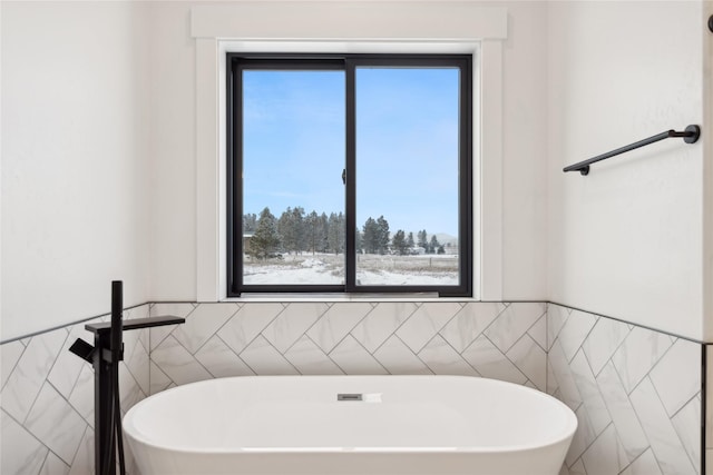 bathroom featuring a soaking tub, wainscoting, and tile walls