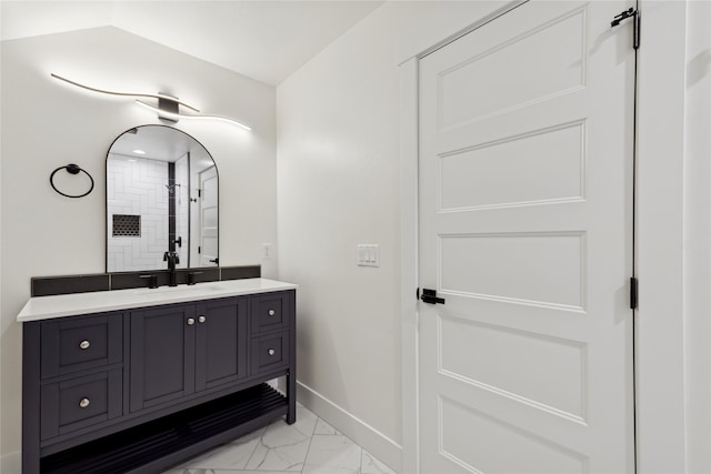 bathroom featuring marble finish floor, a tile shower, vanity, and baseboards