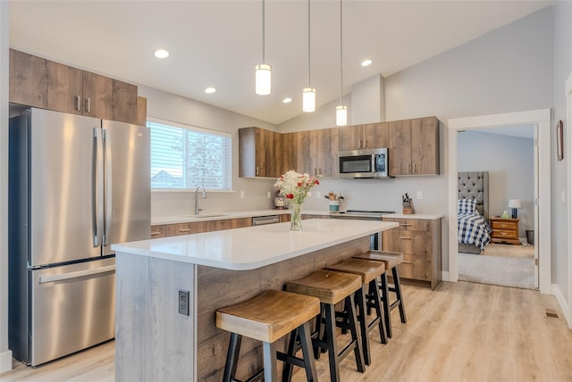 kitchen featuring a center island, pendant lighting, vaulted ceiling, a kitchen bar, and appliances with stainless steel finishes