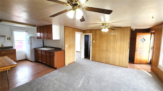 kitchen featuring freestanding refrigerator, a sink, wood walls, a textured ceiling, and dark countertops