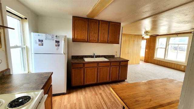 kitchen featuring dark countertops, stove, freestanding refrigerator, brown cabinetry, and a sink