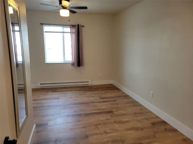 empty room featuring ceiling fan, wood-type flooring, and a baseboard heating unit