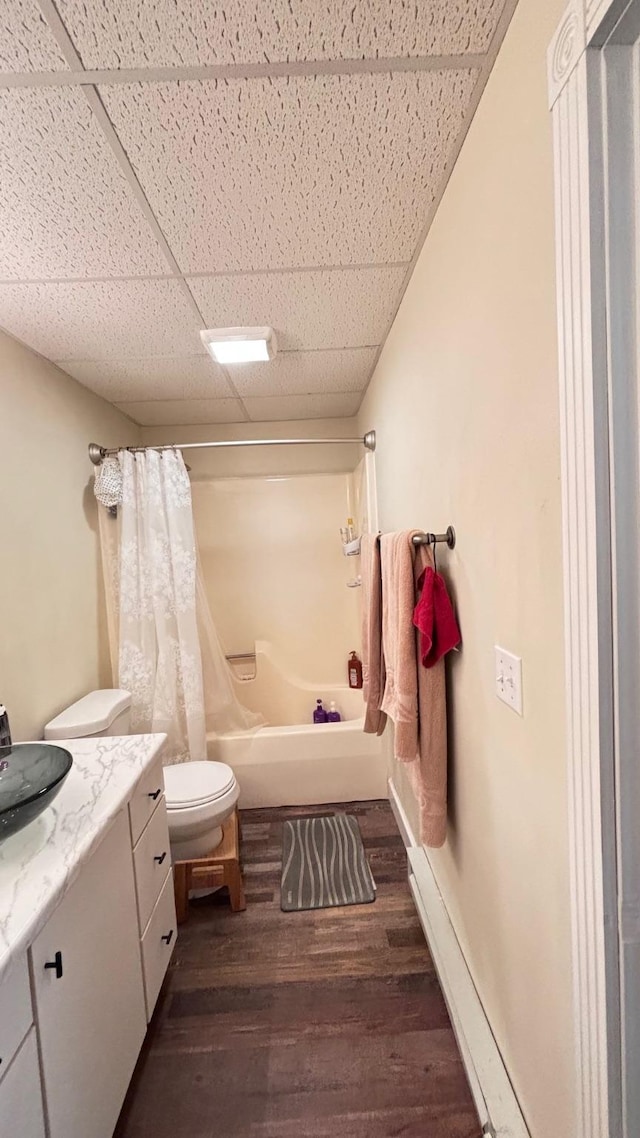 full bathroom featuring a drop ceiling, shower / bathtub combination with curtain, hardwood / wood-style floors, toilet, and vanity