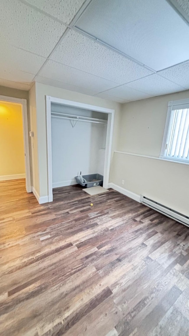 unfurnished bedroom with a paneled ceiling, wood-type flooring, and a closet