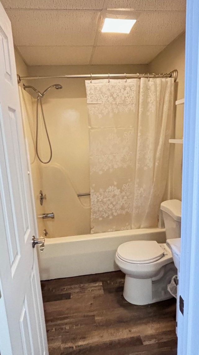 bathroom with hardwood / wood-style floors, a paneled ceiling, shower / bath combination with curtain, and toilet