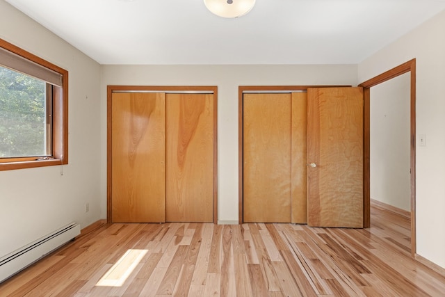 unfurnished bedroom featuring two closets, light wood-type flooring, and a baseboard radiator