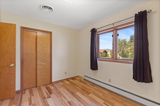 unfurnished bedroom with a closet, light hardwood / wood-style floors, and a baseboard heating unit