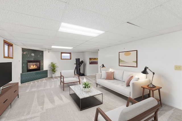 living room with a drop ceiling, light carpet, and a tiled fireplace