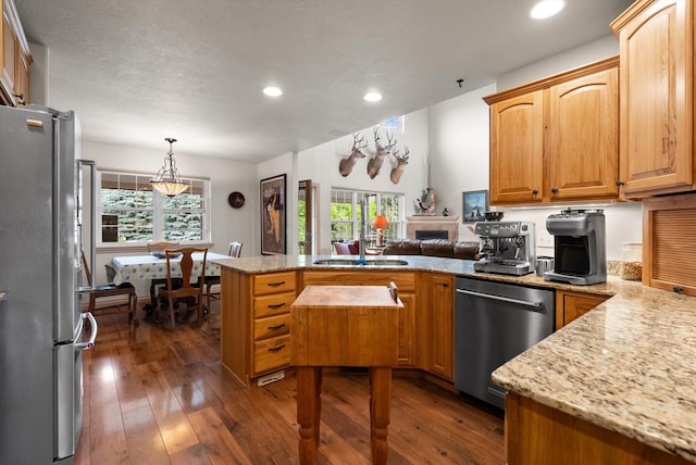 kitchen featuring kitchen peninsula, appliances with stainless steel finishes, dark hardwood / wood-style flooring, light stone counters, and decorative light fixtures