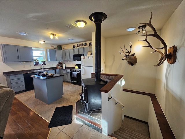 kitchen with gray cabinetry, a center island, sink, light tile patterned floors, and black appliances