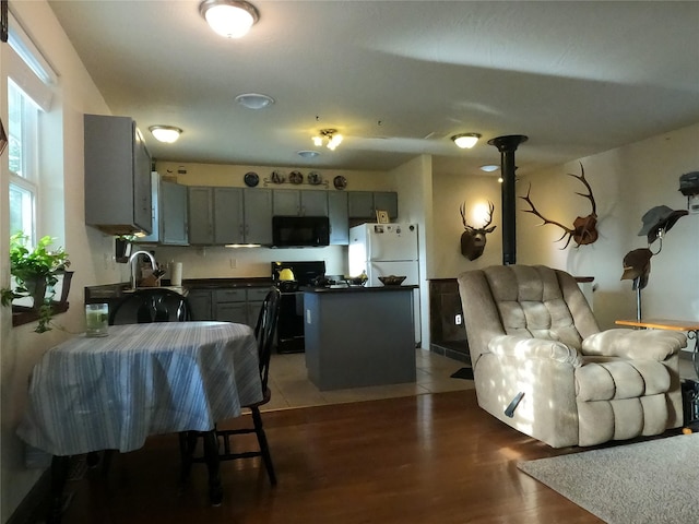 kitchen with gray cabinetry, a center island, black appliances, and dark hardwood / wood-style flooring