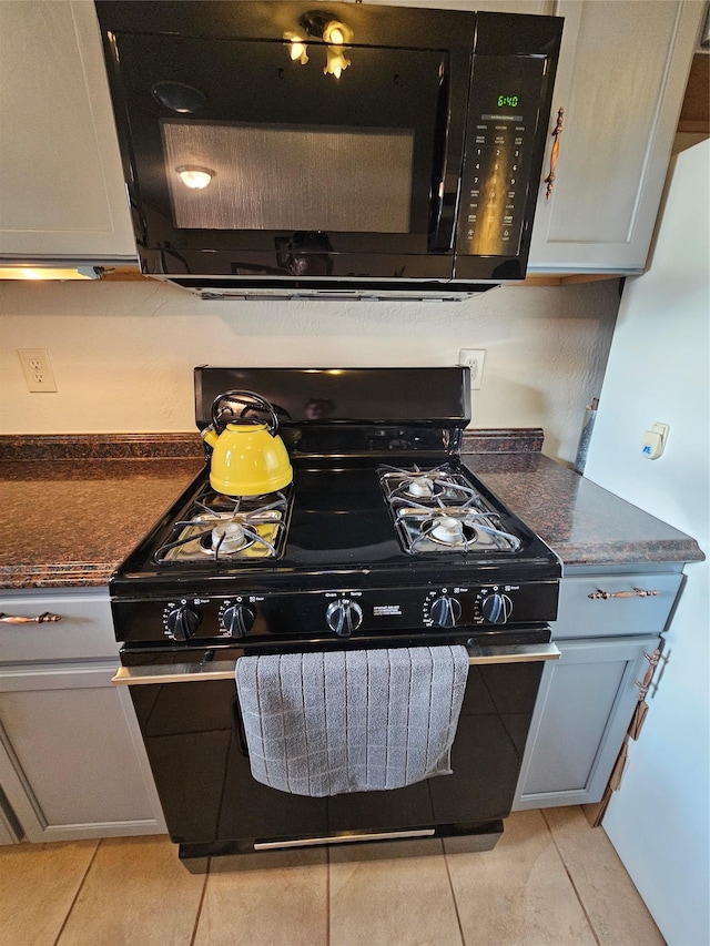 kitchen with dark stone counters, gray cabinetry, light tile patterned floors, and black appliances