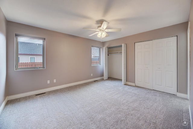 unfurnished bedroom with ceiling fan, light carpet, and multiple closets