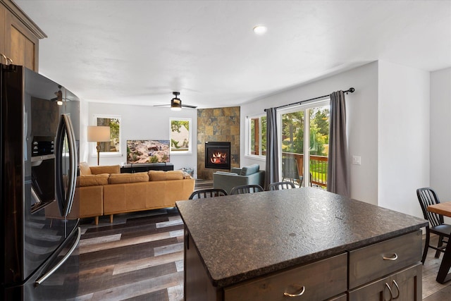 kitchen featuring dark wood finished floors, a center island, stainless steel fridge, a fireplace, and ceiling fan