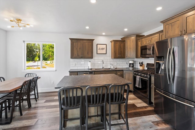 kitchen with dark countertops, backsplash, a center island, appliances with stainless steel finishes, and a sink