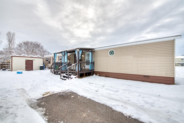 snow covered back of property featuring a storage unit