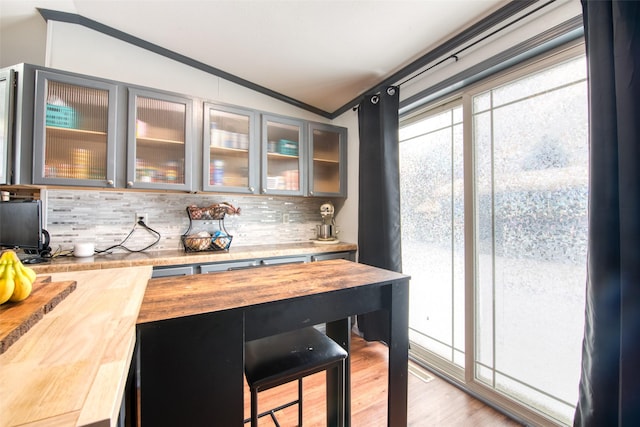 bar featuring vaulted ceiling, light wood-type flooring, tasteful backsplash, and butcher block countertops