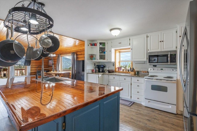 kitchen featuring appliances with stainless steel finishes, light wood-type flooring, rustic walls, blue cabinetry, and white cabinetry