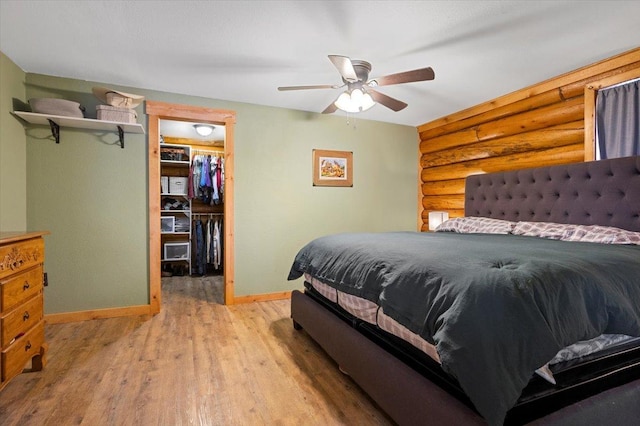 bedroom with ceiling fan, log walls, light hardwood / wood-style flooring, a walk in closet, and a closet