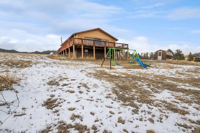 snow covered house featuring a playground, a deck, and a storage shed