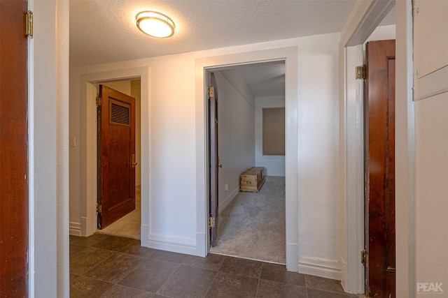 corridor featuring a textured ceiling and dark colored carpet