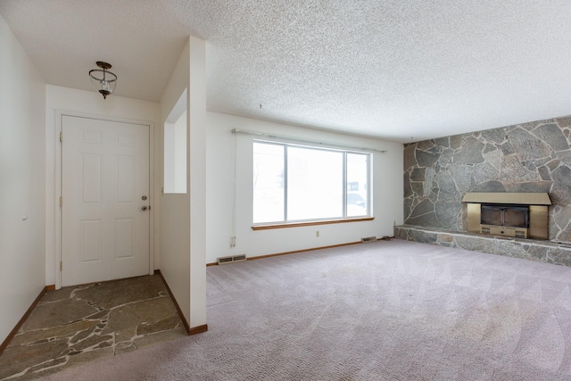 unfurnished living room featuring carpet flooring, a textured ceiling, and a stone fireplace