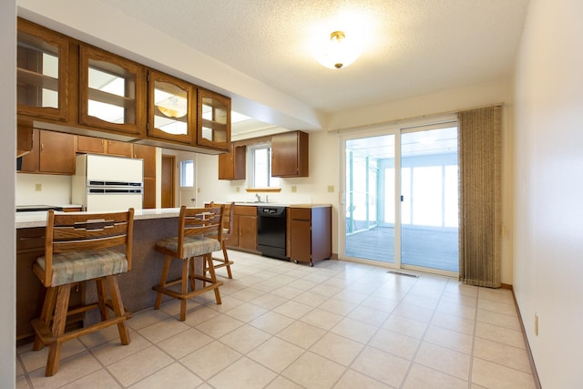 kitchen featuring a textured ceiling, white refrigerator, dishwasher, a breakfast bar area, and light tile patterned flooring