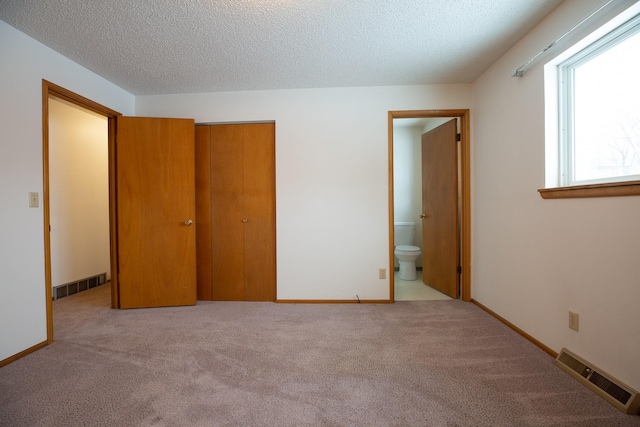 unfurnished bedroom featuring a textured ceiling, ensuite bath, light carpet, and a closet