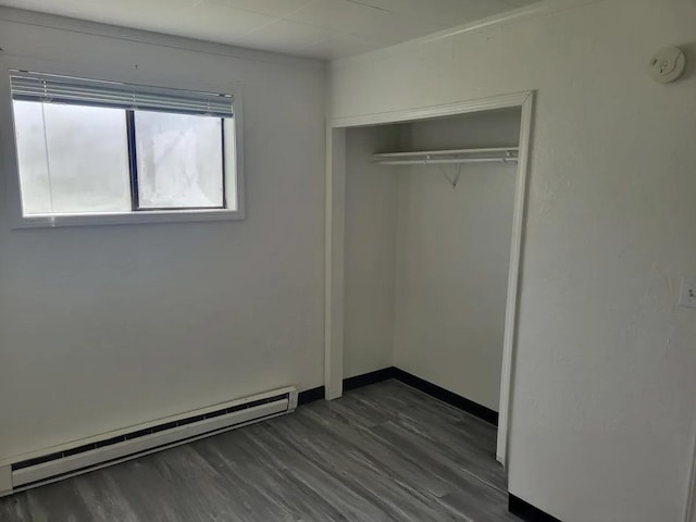 unfurnished bedroom featuring a closet, baseboard heating, and dark wood-type flooring