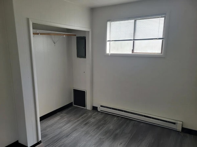 unfurnished bedroom featuring dark hardwood / wood-style flooring, baseboard heating, electric panel, and a closet