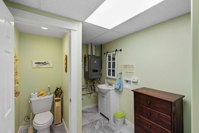 bathroom featuring a paneled ceiling, vanity, tankless water heater, and toilet