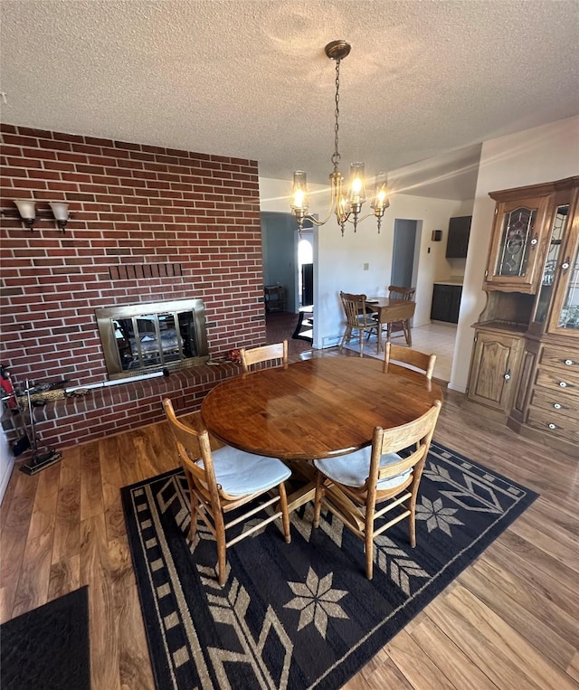 dining area featuring a fireplace, hardwood / wood-style floors, a textured ceiling, and a notable chandelier