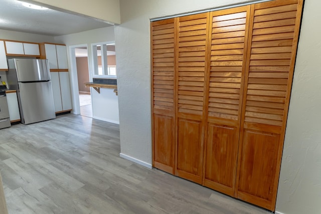 interior space with a textured wall, light wood finished floors, and baseboards