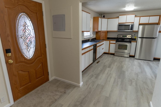 kitchen featuring light wood finished floors, dark countertops, a sink, appliances with stainless steel finishes, and white cabinetry